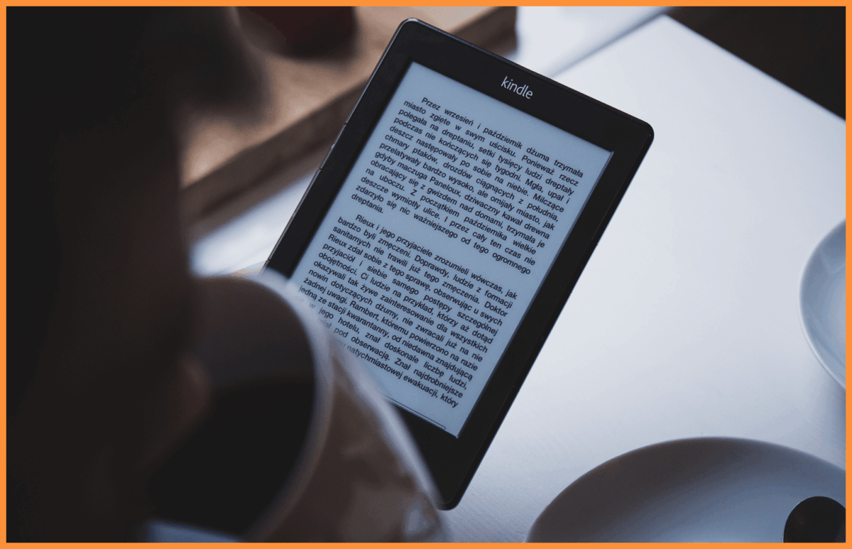 Osoba czyta na czytniku Kindle, trzymając filiżankę kawy, w pomieszczeniu.