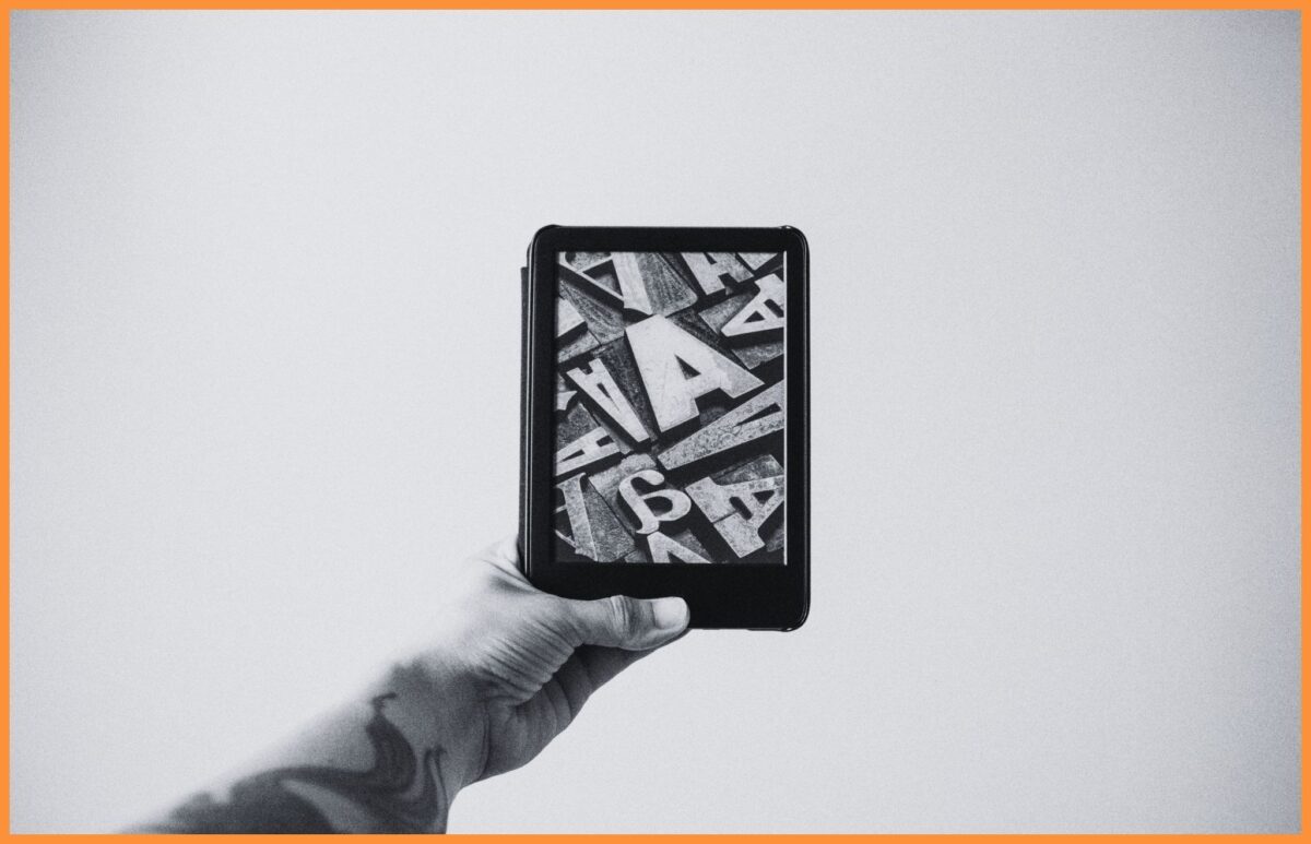 Czarno-biała fotografia przedtsawiająca wytatuowaną dłoń trzymającą e-czytnik Kindle.
