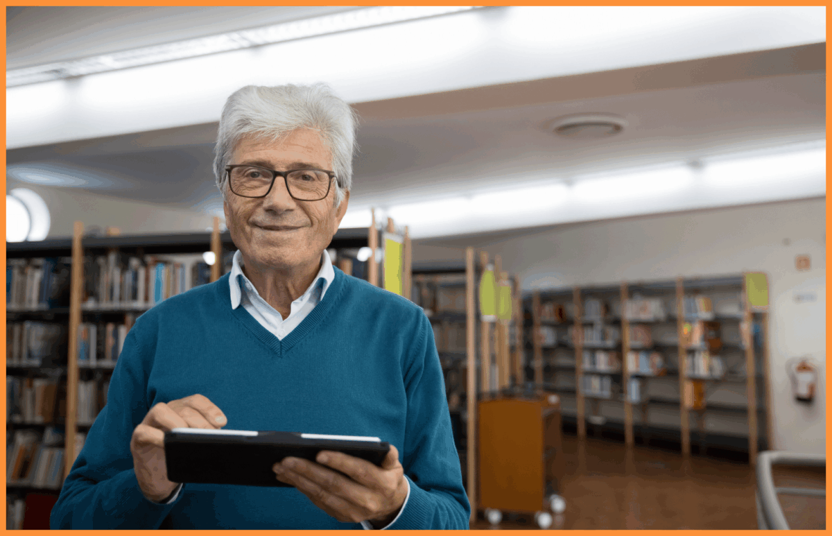 Starszy Pan trzymający czytnik e-booków w bibliotece 