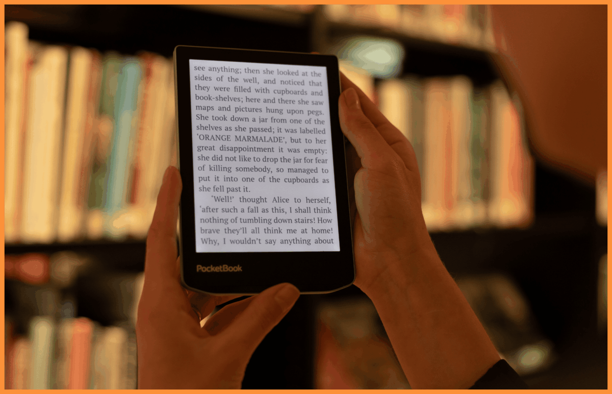 Kobieta trzymająca w rękach czytnik e-book z ekranem E ink marki PocketBook na tle regałów z książkami