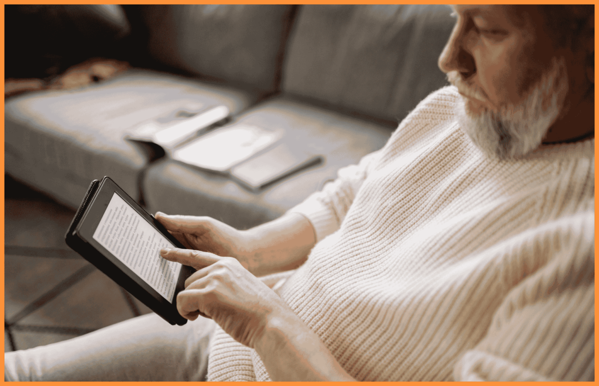 Mężczyzna z brodą, ubrany w biały sweter, czytający e-book na czytniku E-Ink.