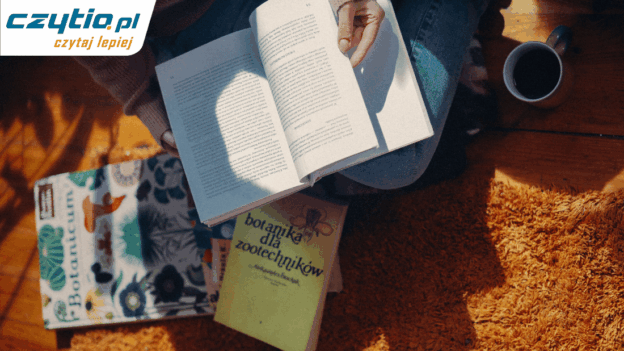 Osoba siedąca na pomarańczowym dywanie, obok kubka z herbatą, czytająca ksiązki i publikacje naukowe.